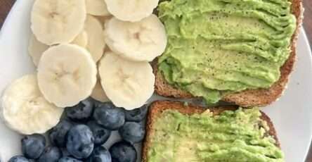Healthy avocado toast on whole wheat bread served with banana slices and fresh blueberries on a simple breakfast plate.