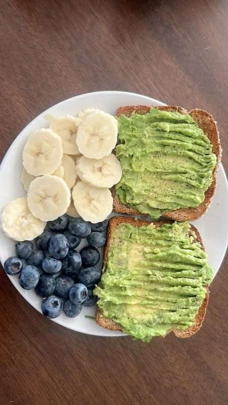 Healthy avocado toast on whole wheat bread served with banana slices and fresh blueberries on a simple breakfast plate.